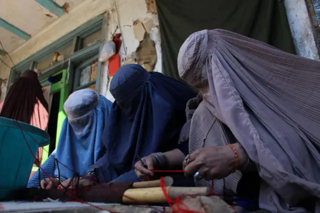 Afghan women work wearing Burqas covering their faces entirely at a carpet loom at a home in Kandahar, Afghanistan