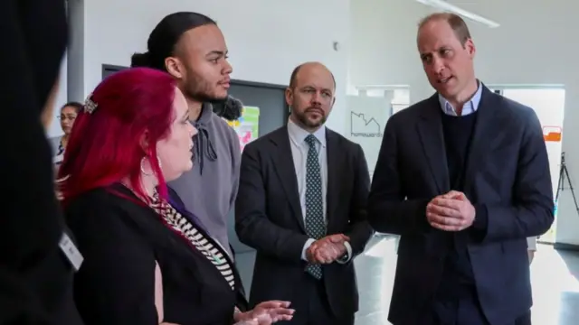 Prince William pictured standing with his hands collapsed together while engaged in conversation with three others