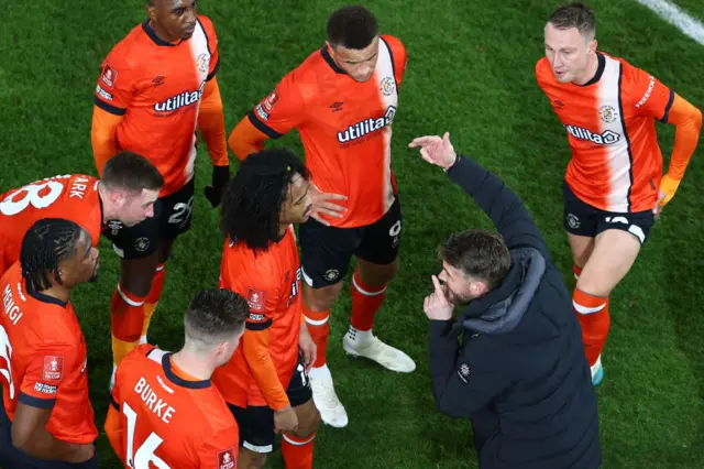 Rob Edwards addresses his Luton players on the side of the pitch.