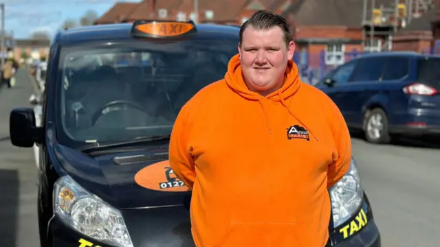 Shaine Ashley Tench stands in bright orange hoodie in front of his taxi