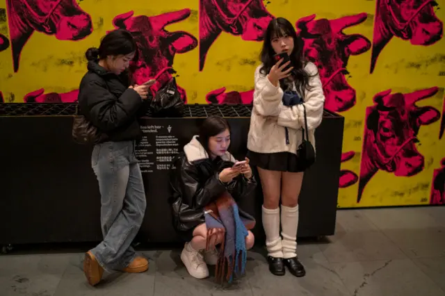 Three women check their iPhones at the Museum of Modern Art on November 21, 2023 in New York City