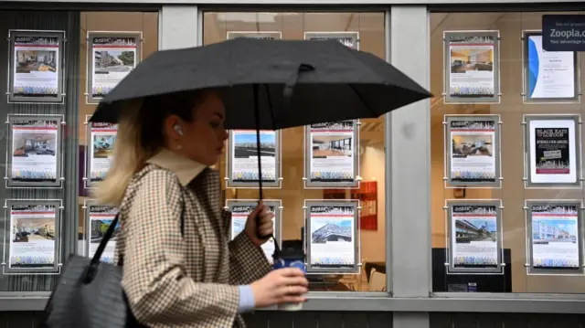 A woman walks past properties advertised at an estate agent's in London