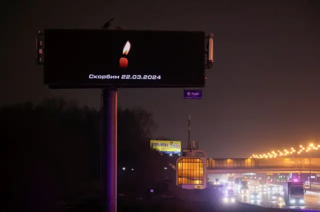 A digital billboard opposite the concert venue reads "We mourn" and the date of the attack