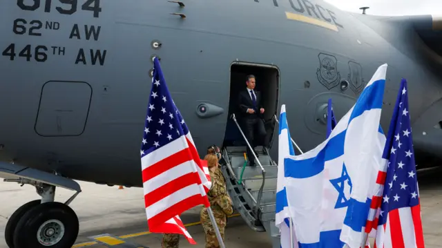 American and Israeli flags are in the foreground, Antony Blinken disembarks a plane in the background