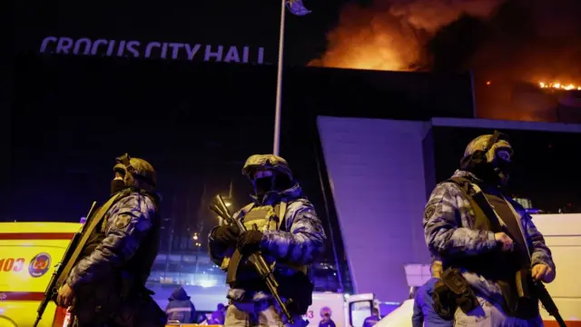 Russian law enforcement officers stand guard near the burning Crocus City Hall concert venue following a reported shooting incident, outside Moscow, Russia, March 22, 2024.