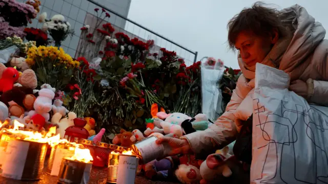 A woman lights a candle at a makeshift memorial made of flowers and soft toys