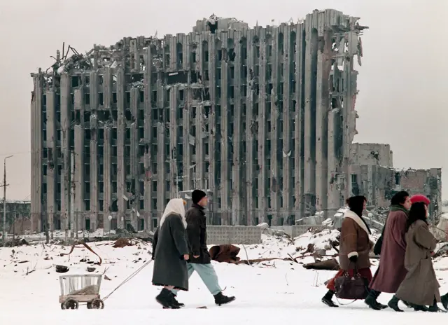 Chechens walk past buildings in Grozny shattered in the first Chechen war