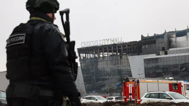 An officer holding a gun stands near the fire-damaged Crocus City Hall