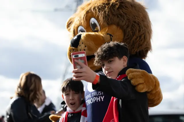 Fans take a selfie with the SPFL Trust Trophy Mascot during the SPFL Trust Trophy Final match between The New Saints and Airdrieonians at Falkirk Stadium, on March 24, 2024, in Falkirk, Scotland.