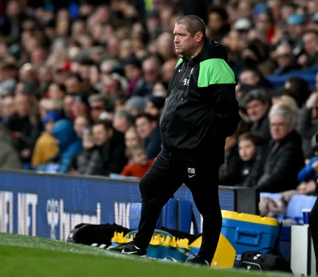 Matt Beard stands with his hands in his pockets on the touchline