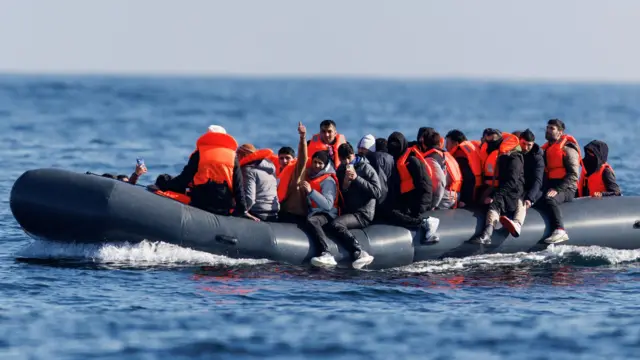 Migrants gesture and take pictures as they cross the English Channel on a small boat