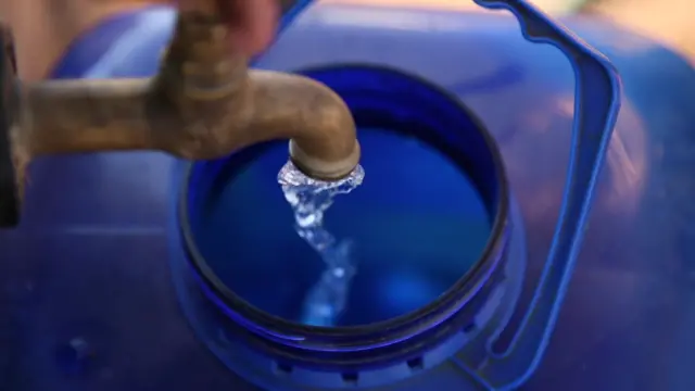 A large water bottle being filled from a tap.