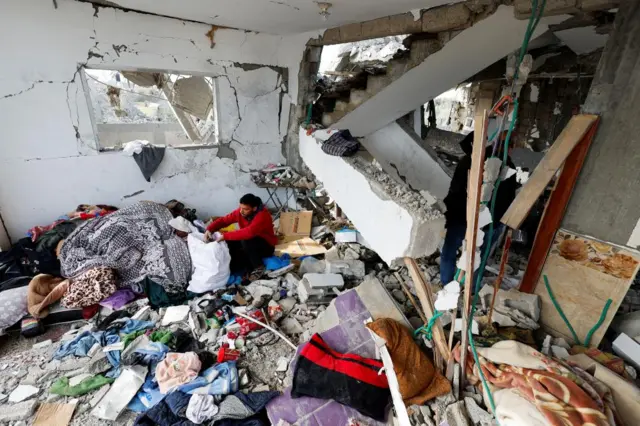 A Palestinian man in Rafah sits surrounded by rubble in the remnants of his home as he attempts to salvage some belongings