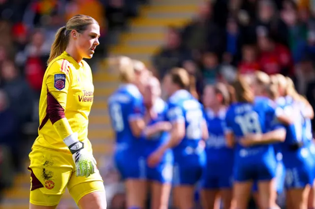 Mary Earps walks back to her goal as Everton celebrate in the background.g