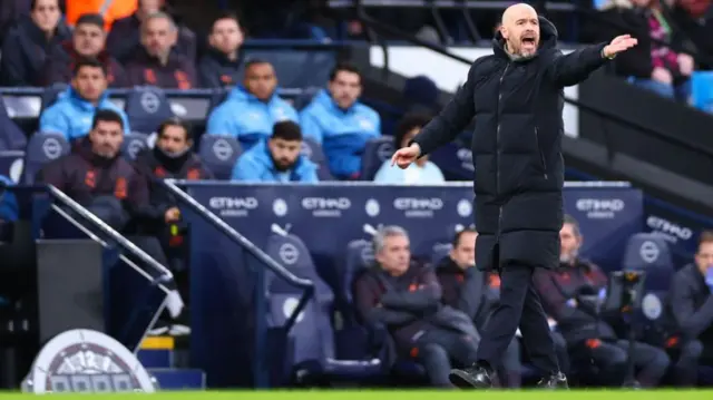 Erik ten Hag stands on the touchline at the Etihad and raises his arm