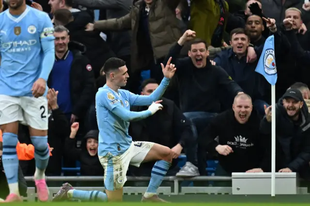 Manchester City fans celebrate as goalscorer Phil Foden takes a knee in front of them