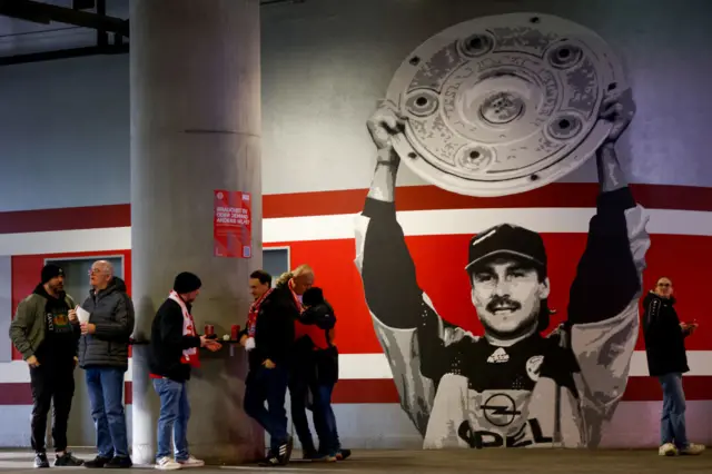 Bayern fans stand with beverages in the Allianz concourse.