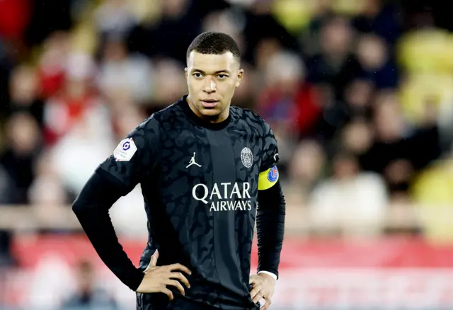 Mbappe stands with his hands on his hips.