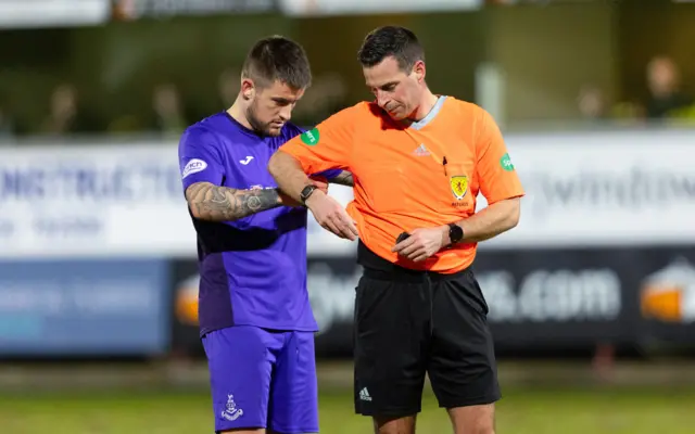 Airdrie Player-Manager Rhys McCabe helps referee Duncan Williams with his communications equipment during a cinch Championship match between Dunfermline and Airdrieonians