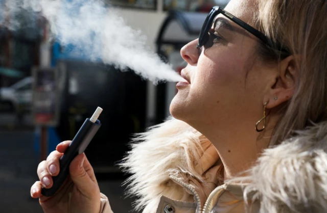 A woman holds an e-cigarette as she vapes on a street in Manchester