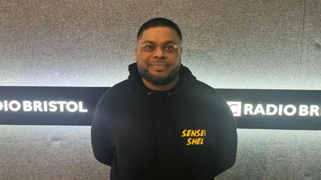 Shelim Ali standing in the Radio Bristol studio wearing a black hoodie