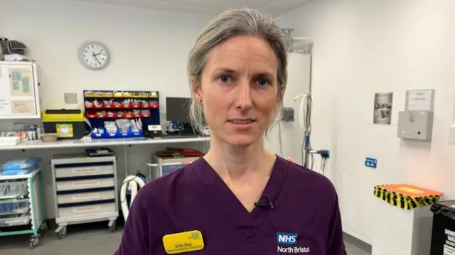 Ellie Day standing in an emergency department room wearing her purple scrubs and a name tag