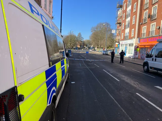 The side of an ambulance on the road where a police cordon has sectioned off a large area of the road