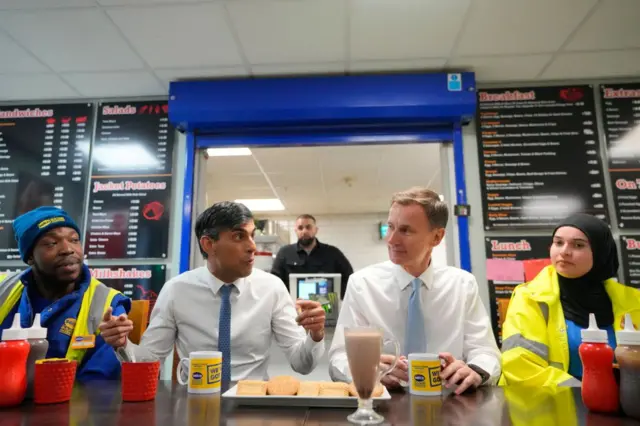 Sunak and Hunt have a drink and biscuits with employees during a visit to a builders warehouse