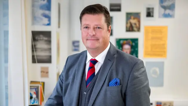 Sir Martyn Oliver, wearing a grey suit and red and blue tie