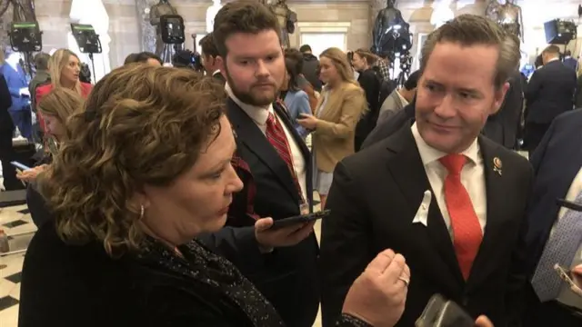 Woman speaking in statuary hall with next to man in red tie