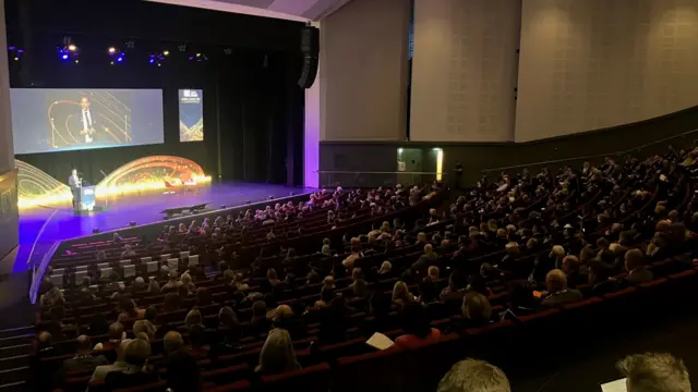 John Camp on stage, seen from the back of the hall