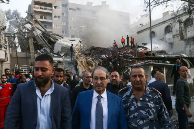 Syrian Foreign Minister Faisal Miqdad (centre) stands with a man either side of him as he inspects the scene of the strike