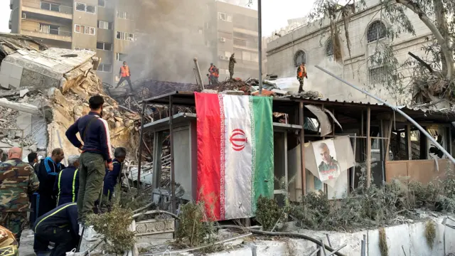 An Iranian flag hangs as smoke rises after what the Iranian media said was an Israeli strike on a building close to the Iranian embassy in Damascus, Syria