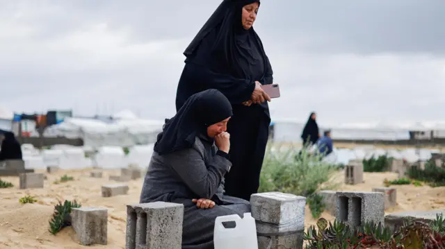 Palestinian women visit graves of people who were killed in the ongoing conflict between Israel and Hamas