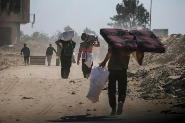 Families walk carrying belongings on a rubble-strewn road in Khan Younis