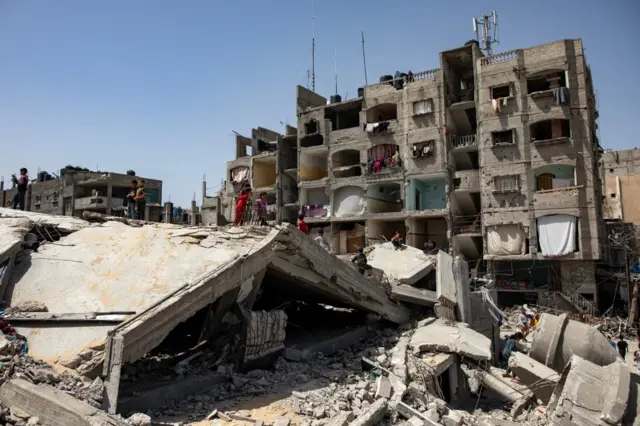 Displaced Palestinians stand on the wreckage of a building in Rafah, southern Gaza on 5 April