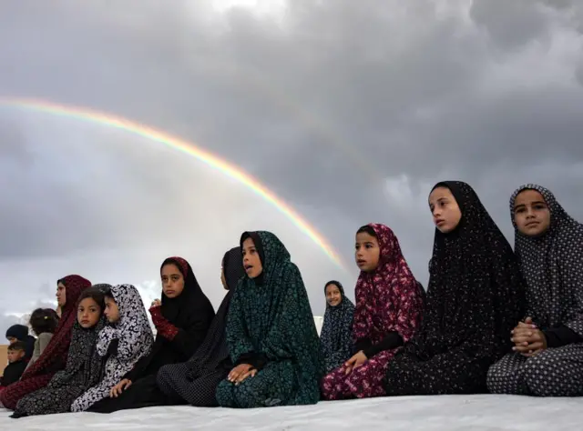 Girls perform prayers underneath a rainbow