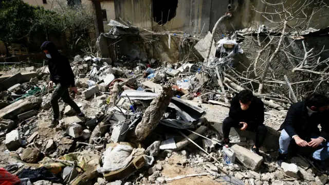 People sit on rubble at the site of an airstrike in Habbariyah, southern Lebanon