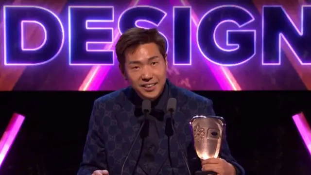 A man in a blue patterned suit smiles as he holds a Bafta