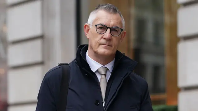 Image of David Smith - wearing glasses and rain coat - on his way into the inquiry