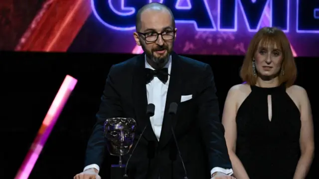 A man and a woman stand at the Bafta lectern