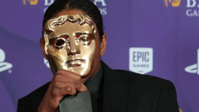 Nadji Jeters holds his Bafta award up to his face, so that the golden mask obscures his face completely