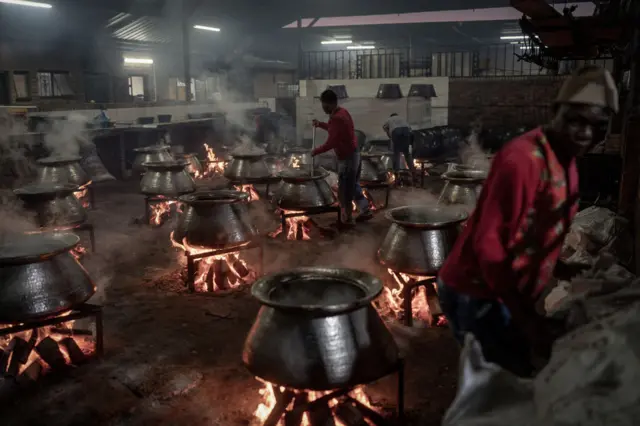 Several large pots of food cooking over a fire in a large room in Cape Town, South Africa