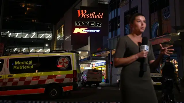 A report does a live stand up outside the Sydney mall where a mass stabbing event took place