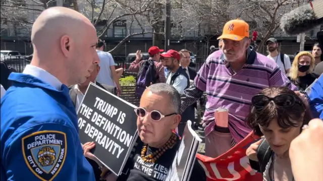 Protesters stand outside the Manhattan courtroom with signs criticising Donald Trump