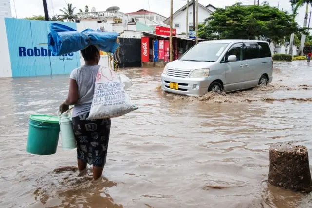 A woman attempts to cross the street in the Msasani neighbourhood on March 13, 2017 in Dar es Salaam as heavy rains flooded many low-lying parts of the capital.