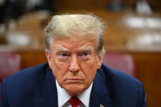 Donald Trump in a Manhattan courtroom in closeup, dressed in a blue suit and red tie.