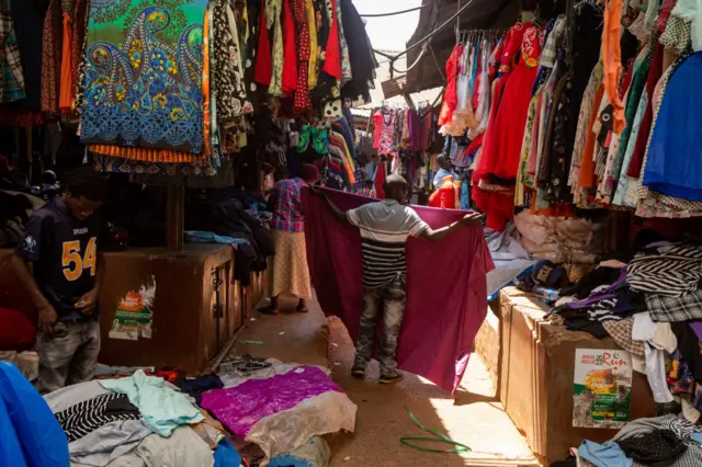 A seller organises second-hand textile items at his stall while waiting for costumers at a market in Kampala on October 7, 2023.