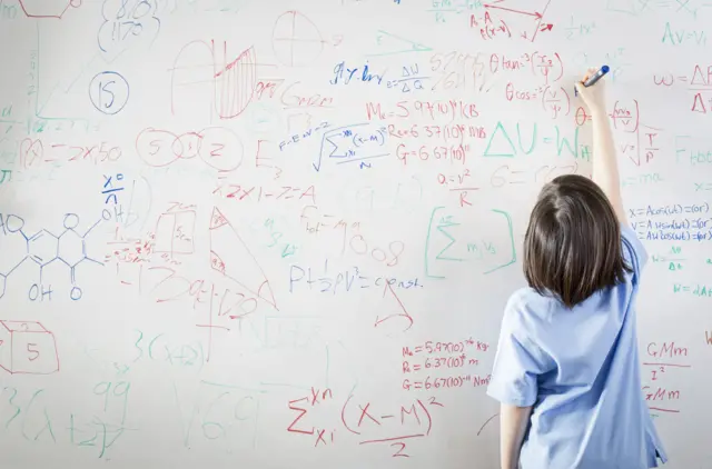 A girl writes on a whiteboard covered in complicated mathematical equations