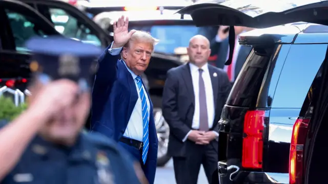 Donald Trump waves as he walks towards a black SUV